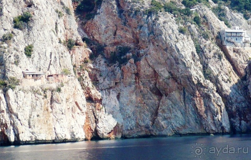 В южной части Афона очень много так называемых исихастерий – одиночных жилищ монахов, которые ведут уединенный, отшельнический образ жизни. Если присмотреться, видно, как их избушки цепляются за края утеса. Смотрите, на снимке слева. Вот этот вот канат, всё, что связывает аскета с цивилизацией. По канату переправляются продукты и вещи для отшельника. 