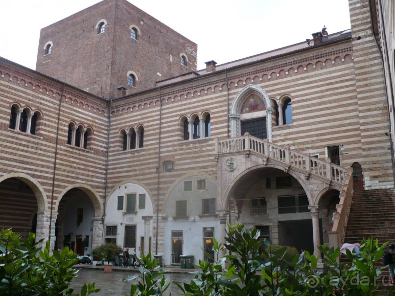 Мы заходим во Двор Старого рынка. Здесь привлекает внимание Лестница делла Раджоне, сооруженная в XV веке. Двор в романском стиле окружают фасады с полукруглыми арками и благородными тройными окнами. Белёсые пятна на снимках остались от запотевшего после дождя объектива. Вы не обращайте на них внимание. Всё равно, других то снимков у меня нет. Так что приходится выставлять эти – с пятнами