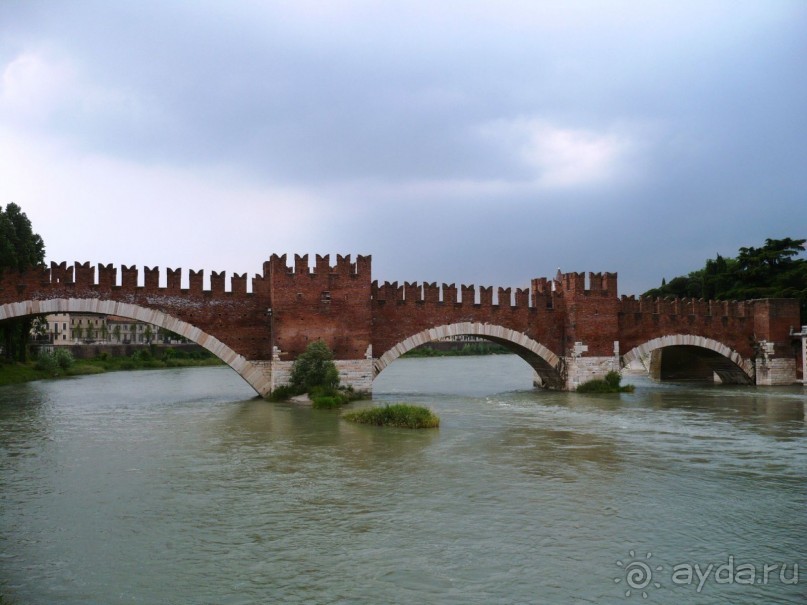 Ещё один великолепный по своей красоте мост предстал пред нашими очами – Понте Скалиджеро. Обратили внимание на зубцы? Как в нашем Московском Кремле. Этот мост представляет собой уникальный образец средневекового укрепленного моста из кирпича с зубцами и проходами, возведенного с целью защиты замка. Да он, собственно, и есть небольшой замок на реке. Его так же, как и Каменный мост, взорвали фашисты при своём отступлении. Но вскоре после войны мост был восстановлен с использованием всех обнаруженных фрагментов.

Это было последним, что мы увидели перед ужасным ливнем, который вскоре обрушился на город. Экскурсовод, как ни в чем не бывало, под потоками низвергающихся вод продолжала вести экскурсию. Да и мало того, в самую кульминацию грозы, мы, как идиоты, шествовали по открытому мосту через Адидже.
