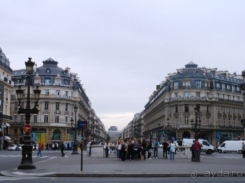 А это вид на улицу, если повернуться к театру спиной. Она называется Avenue de L’Opera. Некоторые улицы  называются авеню, а некоторые рюи (rue). Например, Rue La Fayette. Вдали уже видны характерные крыши Большого Лувра. Но туда мы придем позже. 