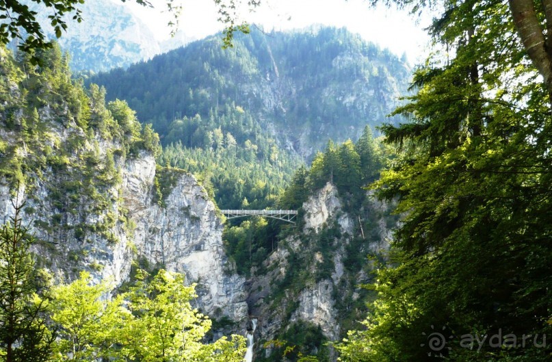 Окрестности замка просто изумительны. Примечателен мост Марии. Он переброшен через ущелье Пеллат. Это висячий мост, который старше замка Нойшванштайн, пересекает ущелье на высоте 92м над 45-метровым водопадом. Он назван в честь матери короля Людвига II, королевы Марии, принцессы Прусской. Экскурсовод рассказывала, что по этому мосту очень просто дойти пешком до Австрии. Сейчас же все границы внутри стран Евросоюза отменены. Так что сам не заметишь, как окажешься в другой стране. У нее был случай, когда один мужчина из ее группы перешел мост и углубился в горы. Когда он позвонил с просьбой помочь ему вернуться, оказалось, что он уже давно находится в Австрии. 