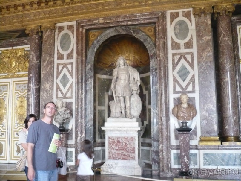 История Версальского дворца берет своё начало с 1623 г. Людовик XIII строит очень скромный охотничий замок наподобие феодального, из кирпича, камня и кровельного сланца.
Созданием Большого Версаля человечество обязано Людовику XIV. С  1661 «король-солнце» начал расширять дворец для того, чтобы использовать его как свою постоянную резиденцию. Строительство Версальского дворца шло 50 лет и  завершилось в 1710 году. Участок будущей постройки потребовал огромного объёма земельных работ. 
Рекрутирование рабочих с окрестных деревень проходило с большим трудом. Крестьян принуждали становиться «строителями». Чтобы увеличить рабочих на строительстве дворца, король запретил всё частное строительство в окрестностях. Из-за нехватки рабочих часто завозили из Нормандии и Фландрии. 
Почти все заказы велись через тендеры, расходы исполнителей, превышающие изначально названные, не оплачивались. В мирные времена к строительству дворца привлекалась и армия. Министр финансов Жан-Батист Кольбер следил за крайней экономностью. 
То, что сегодня многим кажется невероятной роскошью и расточительством, было построено как можно дешевле, из-за чего впоследствии не работали многие камины, не закрывались окна и жить во дворце зимой было крайне неуютно. Аристократия, за исключением близких родственников королевской семьи, должна была жить в узких каморках под крышей. Её принудительное присутствие при дворе было дополнительной мерой предосторожности со стороны Людовика XIV, обеспечивавшего себе, таким образом, полный контроль над деятельностью аристократии. Только при дворе было возможно получить чины или посты, а кто уезжал, терял свои привилегии.
Вот он – «Король-солнце».
