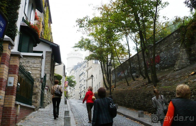 Взойти на Монмартр можно пешком или с помощью фуникулёра. О существовании фуникулера мы узнали уже после посещения Парижа. Поэтому поднимались пешком. Правда, не по знаментиой лестнице, а с обратной стороны холма. Поднялись не очень круто, но довольно утомительно, скажу я вам. Белая башня впереди – это и есть Сакре-Кёр.