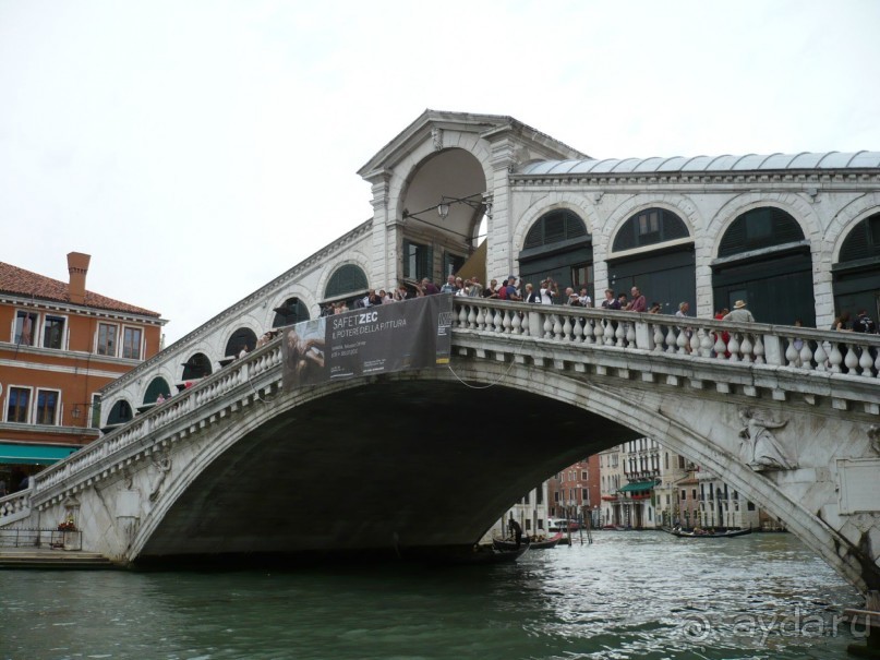 Закончили мы свою экскурсию возле Понте (моста) Риальто на Гранд Канале. 
Это тоже один из символов Венеции. 
Он находится в самом её центре. В разные времена на этом месте строили мосты деревянные, но они гибли во время пожаров, а последняя версия и вовсе обрушилась в 1444 году под тяжестью толпы зевак, собравшихся посмотреть на жену маркиза Феррары.

Каменный Риальто был надежно построен в конце 16 века. Днем на мосту всегда оживленно. Здесь расположены маленькие магазинчики сувениров, кожаных сумок и ювелирных изделий. 
