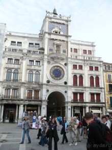 Здесь же стоит Торе дель Оролоджо (Часовая башня). Часы на ней особенные. На циферблате стрелка указывает, в каком зодиакальном знаке сейчас находится наша планета. А собственно само время указывают синие надписи над циферблатом. Слева римскими цифрами показываются часы, а арабскими справа указываются минуты с интервалом в 5 минут. Сейчас на часах 9 часов 30 минут утра. Следующее время, которое они покажут, будет 9 часов 35 минут.