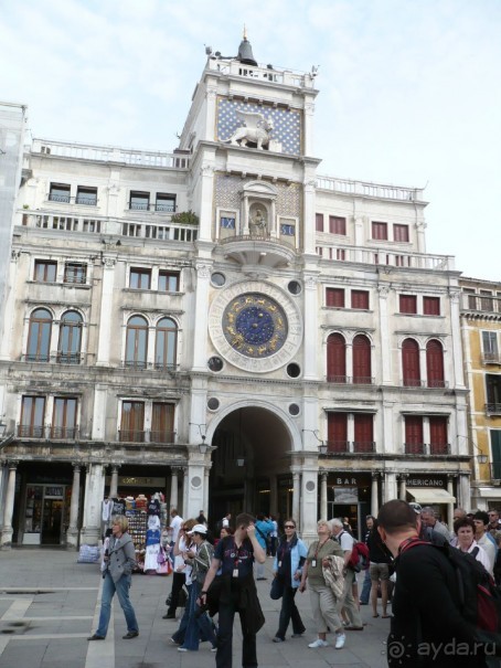 Здесь же стоит Торе дель Оролоджо (Часовая башня). Часы на ней особенные. На циферблате стрелка указывает, в каком зодиакальном знаке сейчас находится наша планета. А собственно само время указывают синие надписи над циферблатом. Слева римскими цифрами показываются часы, а арабскими справа указываются минуты с интервалом в 5 минут. Сейчас на часах 9 часов 30 минут утра. Следующее время, которое они покажут, будет 9 часов 35 минут.