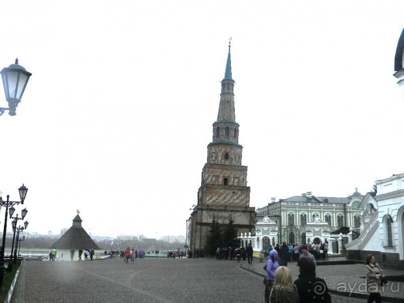 Падающая башня в Казани.  Башня Сююмбике, расположенная внутри Казанского кремля в отдалении от крепостных стен, ранее играла роль сторожевой крепостной башни. С её верхнего яруса открывается хороший обзор рек Казанки и Волги и их окрестностей. Фундамент башни покоится на дубовых сваях, стены выложены из кирпича. Сююмбике состоит из 7 ярусов. Они имеют разную форму: три нижних яруса - квадратные, остальные - восьмиугольные. Два верхних яруса - дозорная вышка и шатёр - увенчаны зелёным шпилем с навершием в виде золочёного "яблока" с полумесяцем. Общая высота башни равна 58 метрам. О времени возникновения Сююмбике точно неизвестно. Самое раннее упоминание о башне в письменных источниках относится к 1777 году, когда она была отмечена на плане кремля. В художественно-публицистической литературе название "Башня Сююмбике" встречается впервые в 1832 году. Постепенно оно стало общеупотребительным. Происхождение башни окутано легендами. По одной из них, башня построена царицей Сююмбике в память о своем муже Сафа-Гирее, умершем в 1549 году.